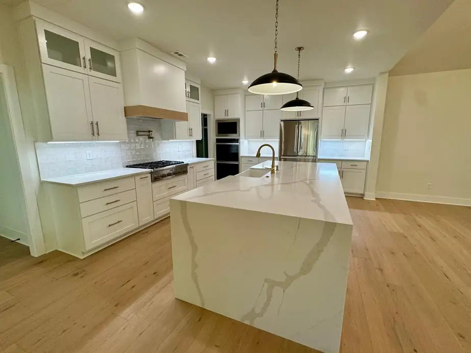 White shaker kitchen with a waterfall quartz island and oak floors, painted by Quality Pro Painting