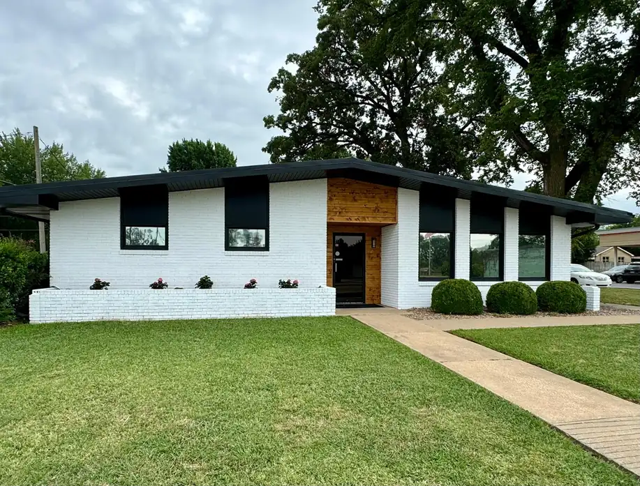 White-painted brick office building with black window surrounds, black eaves and a stained cedar entry, finished by Quality Pro Painting