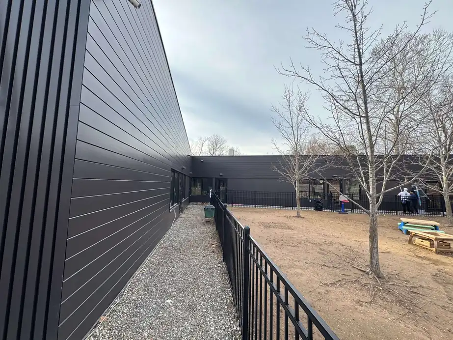 Long charcoal-panel commercial building with a fenced courtyard in Northwest Arkansas