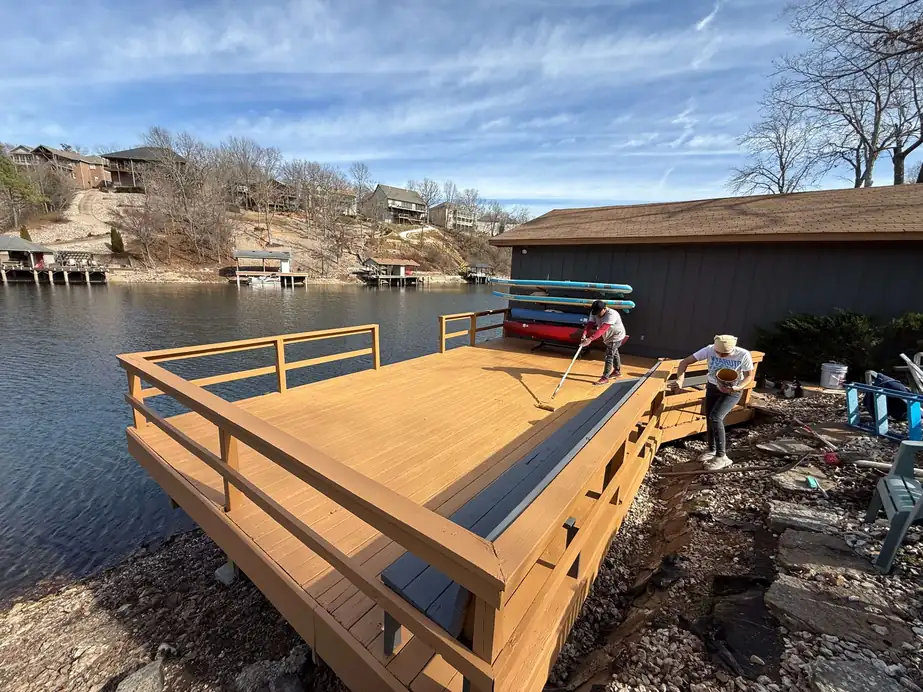 Freshly stained lakeside deck with railing and built-in benches, crew finishing the far end