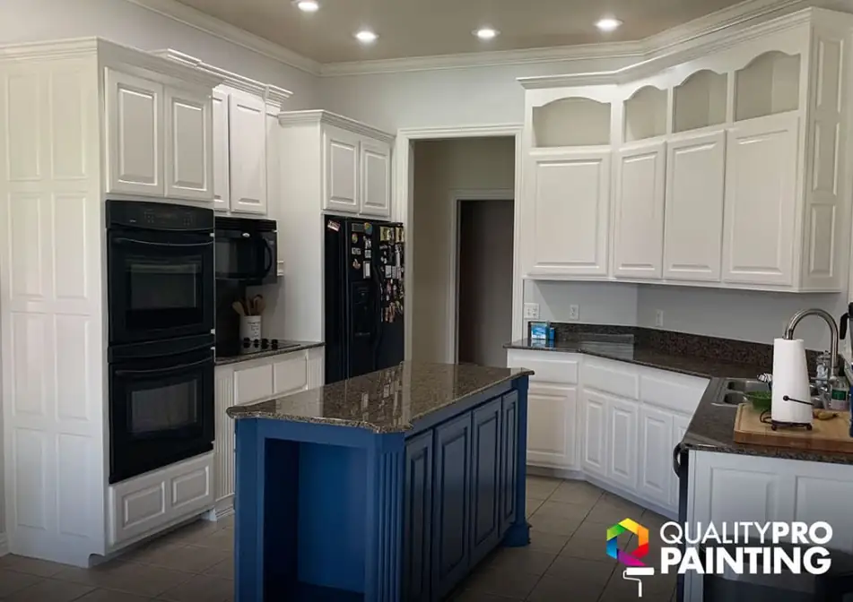 Kitchen with white cabinets and a navy painted island under stone counters