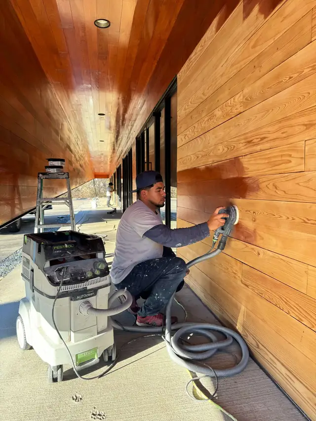 Quality Pro Painting crew member sanding stained cedar siding with a dust-extracted sander