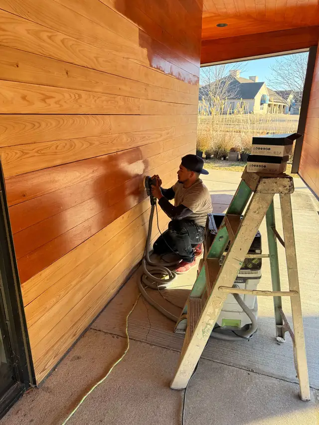 Crew member on a stepladder sanding a cedar porch ceiling