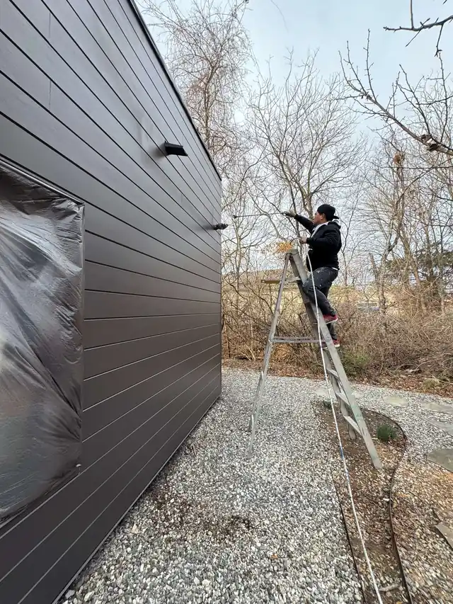 A Quality Pro painter on a ladder at charcoal lap siding