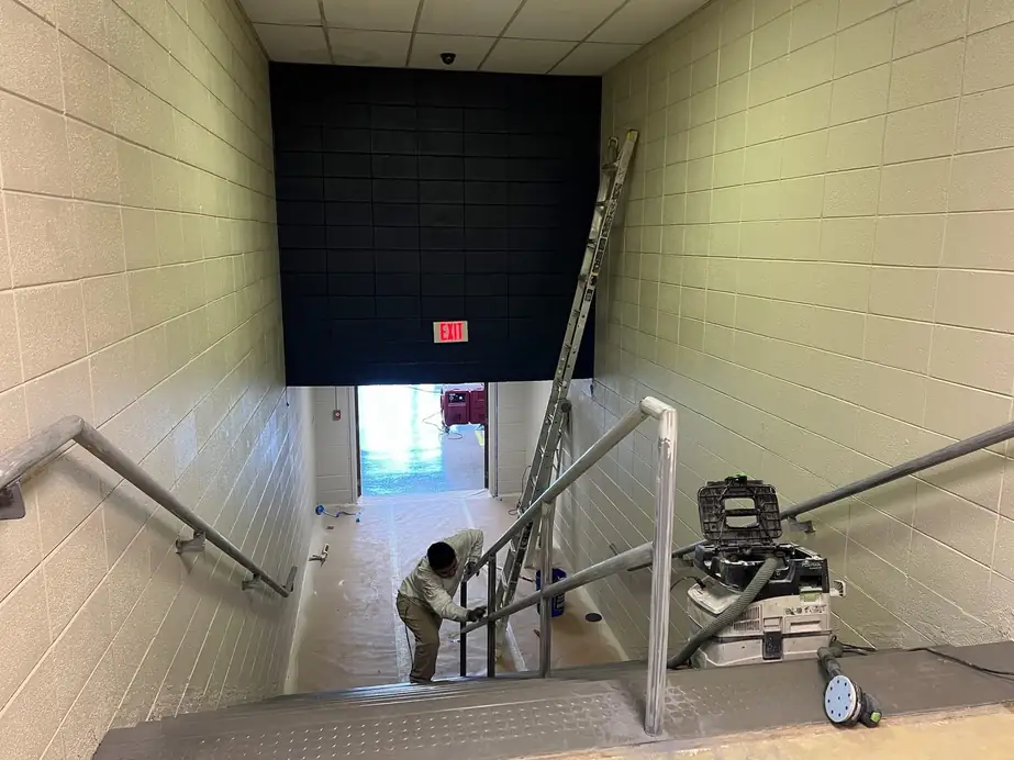 Stairwell with a black-painted back wall and a worker with a ladder at the bottom
